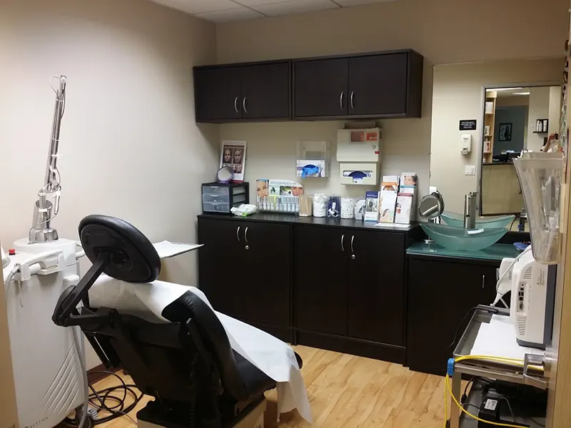 A modern Unified Health dental clinic room features a reclining dental chair with cover, sterilization equipment, dark cabinetry, and various dental tools on the countertop. A sink with a green glass basin is visible, along with brochures and a mirror on the wall.