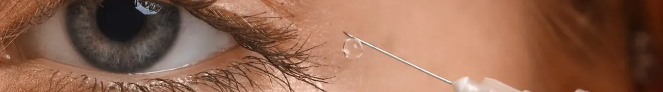 Close-up of a person's eye with a teardrop on the lower lash. A gloved hand holds a syringe with a thin needle near the eye, suggesting the administration of an injection or medical procedure, as if bringing medical care directly into the home environment.
